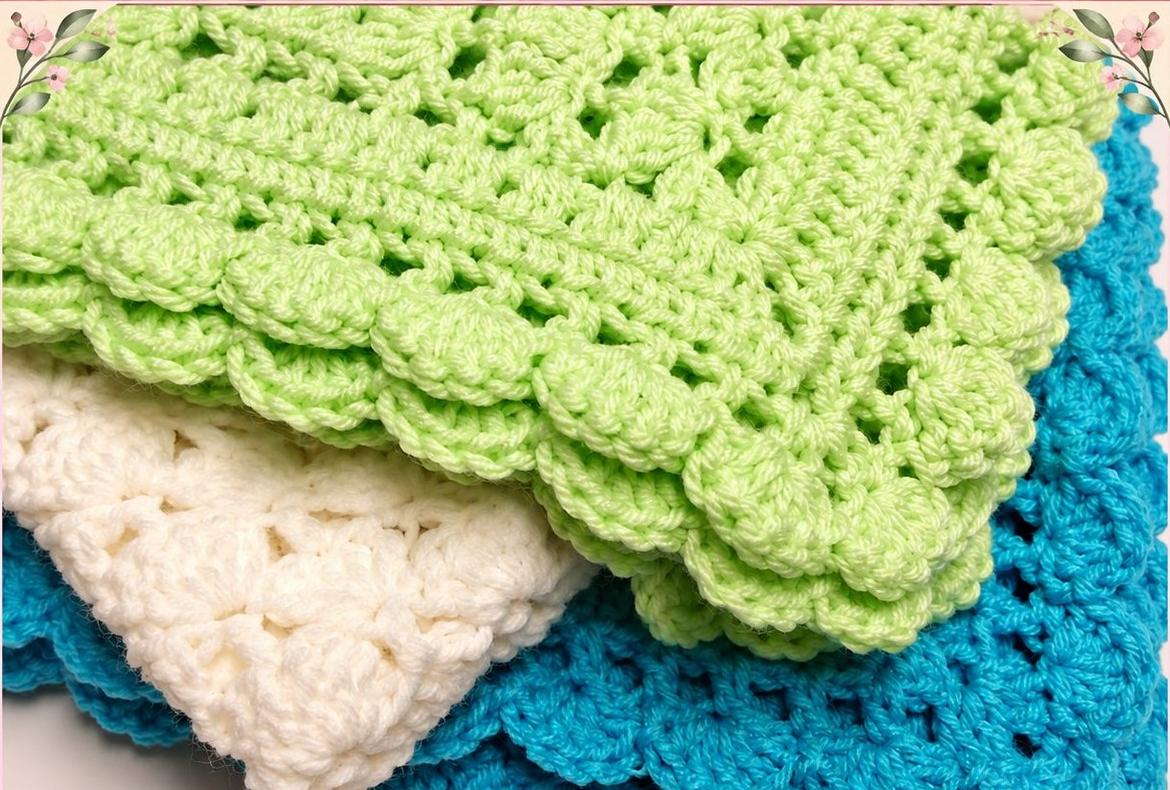 A stack of handmade One Skein Blankets in green, cream and blue, each finished with a scalloped shell-stitch edge